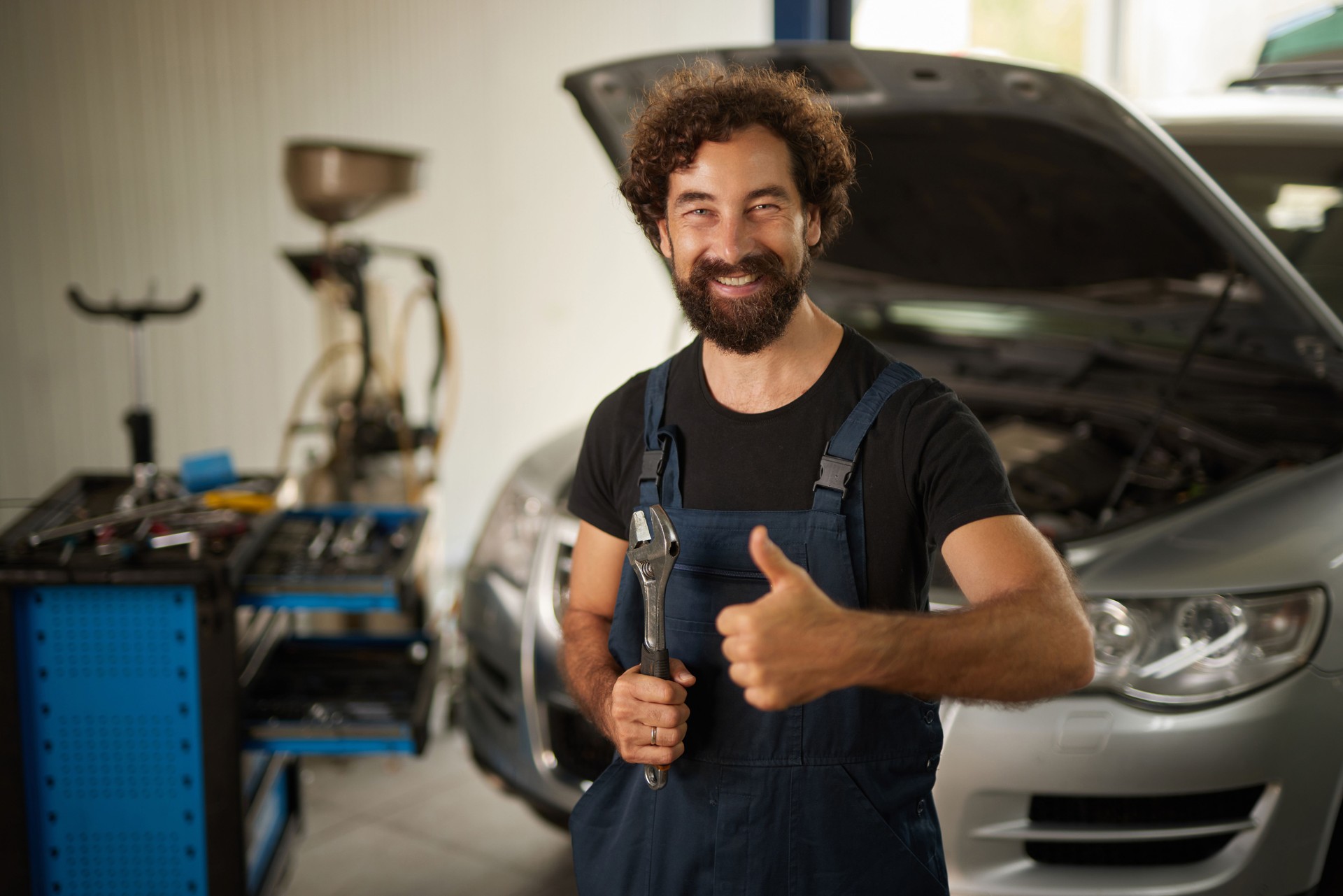 Car mechanic holding wrench and giving thumbs up in auto repair shop