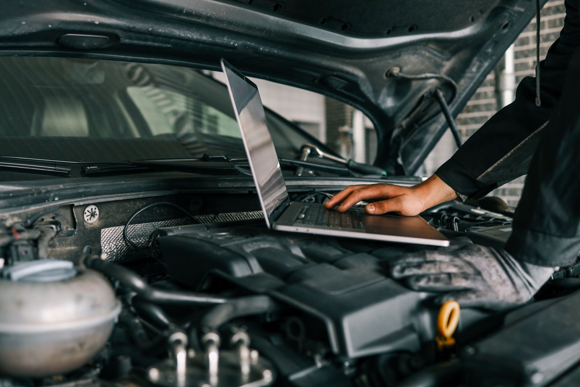 A mechanic using a laptop on a car engine for diagnostics in a garage. Highlights the use of technology in modern vehicle maintenance and repair
