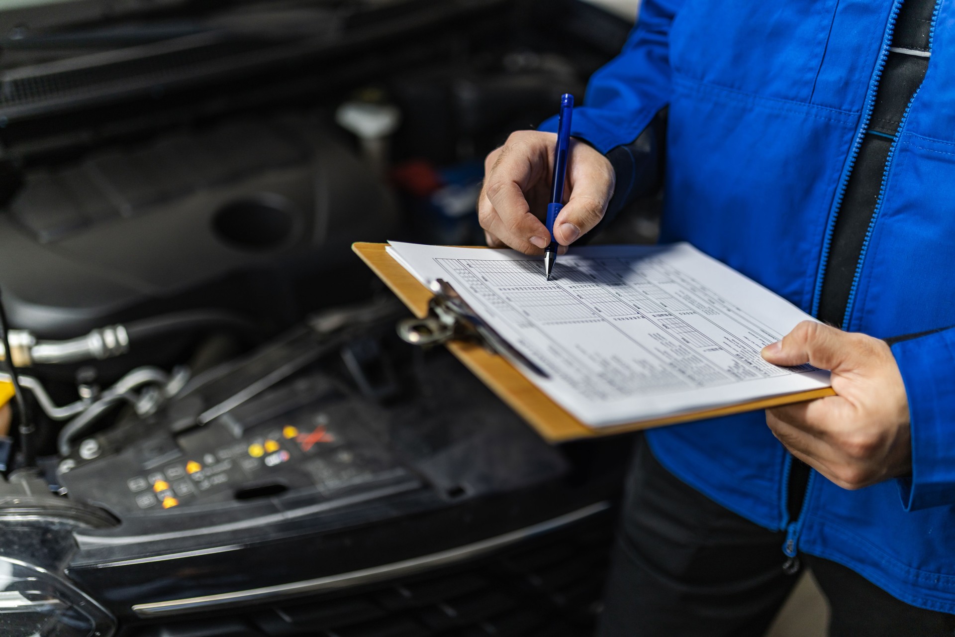 A mechanic inspects a vehicle engine while checking a maintenance checklist in a workshop